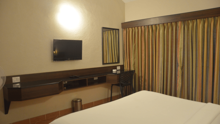 Standard Room at Green Pastures, Kodaikanal featuring a bed, flat TV screen, a dressing table, and a fan.