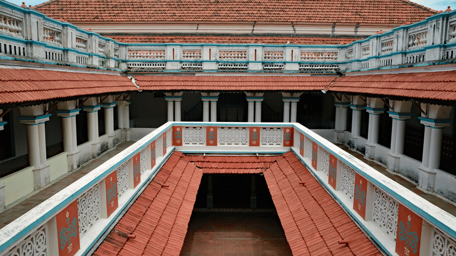Open central courtyard of a Chettinad mansion featuring terracotta-tiled walkways, wooden balconies, and symmetrical heritage architecture surrounding the atrium.