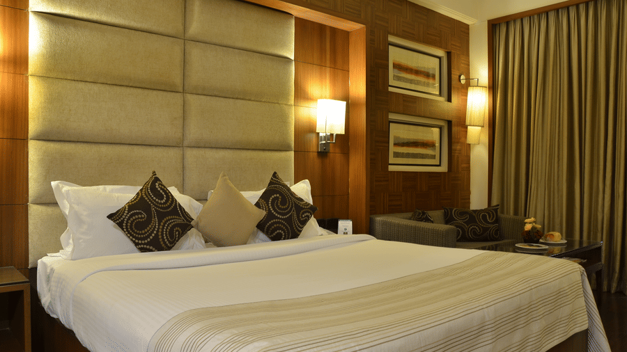 Well lit beddrom at The Bristol Hotel with a king bed, wall mounted lamps and curtained windows.