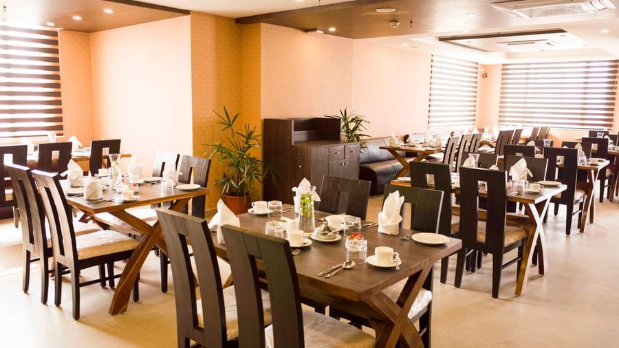 A hotel restaurant dining area with tables set and brown chairs | Daksh The Madhuvan Suites