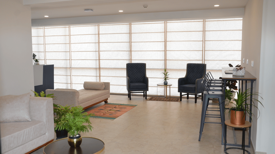 Full view of the lobby area with a sofa, armchairs, coffee table, and large window covered with blinds - Lords Eco Inn Belagavi