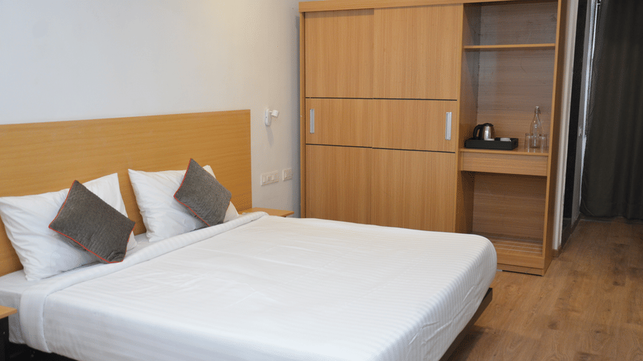 A bedroom featuring a plush double bed, wooden furniture, and neutral decor - Lords Eco Inn Belagavi