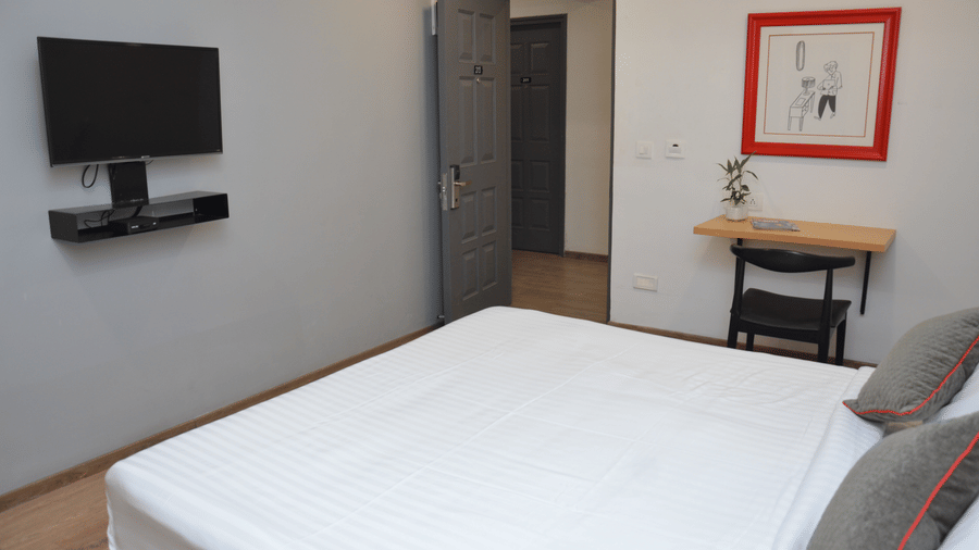 Corner view of a bedroom with a double bed, mounted television, and a framed red picture - Lords Eco Inn Belagavi