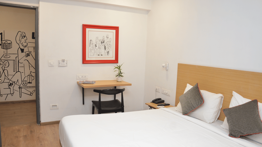 A bedroom with a double bed, bedside table, and a framed picture on the wall - Lords Eco Inn Belagavi