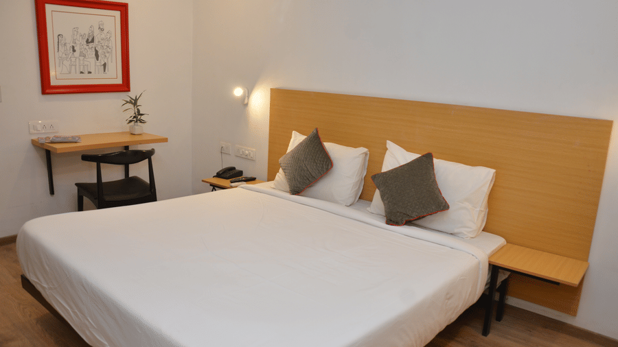 A bedroom featuring a double bed, bedside table, and a framed red picture on the wall - Lords Eco Inn Belagavi