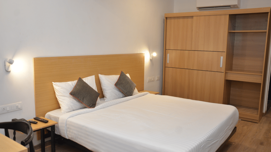 A bedroom with a double bed, bedside table, and a wooden cabinet - Lords Eco Inn Belagavi