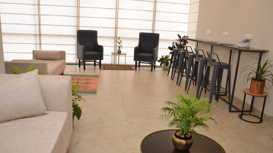 The lobby area at our hotel with a sofa, chairs, coffee table, and large window blinds - Lords Eco Inn Belagavi