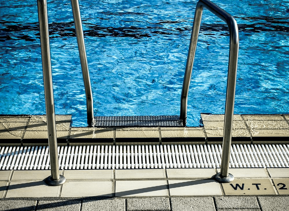 An image of a swimming pool ladder and swimming pool in the background.