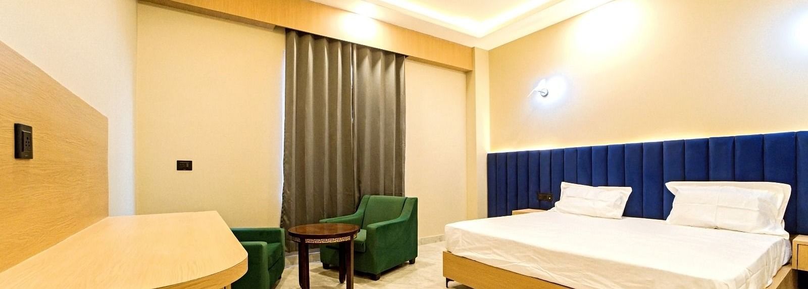 Modern guest room at Grassfield Riveria Resort, Jaipur, featuring a large bed, seating area, ceiling fan, and warm lighting.