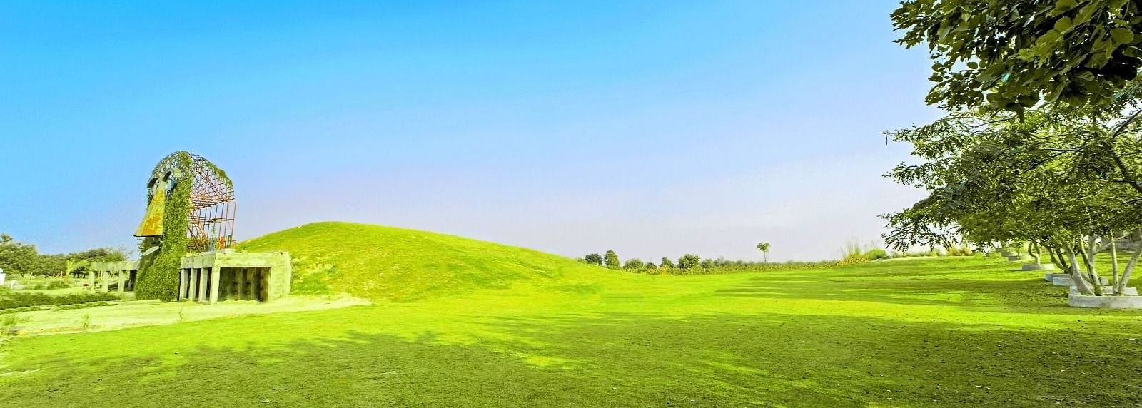 Vast lawn with the artistic mask sculpture of Grassfield Riveria Resort, Jaipur, set against a clear sky.