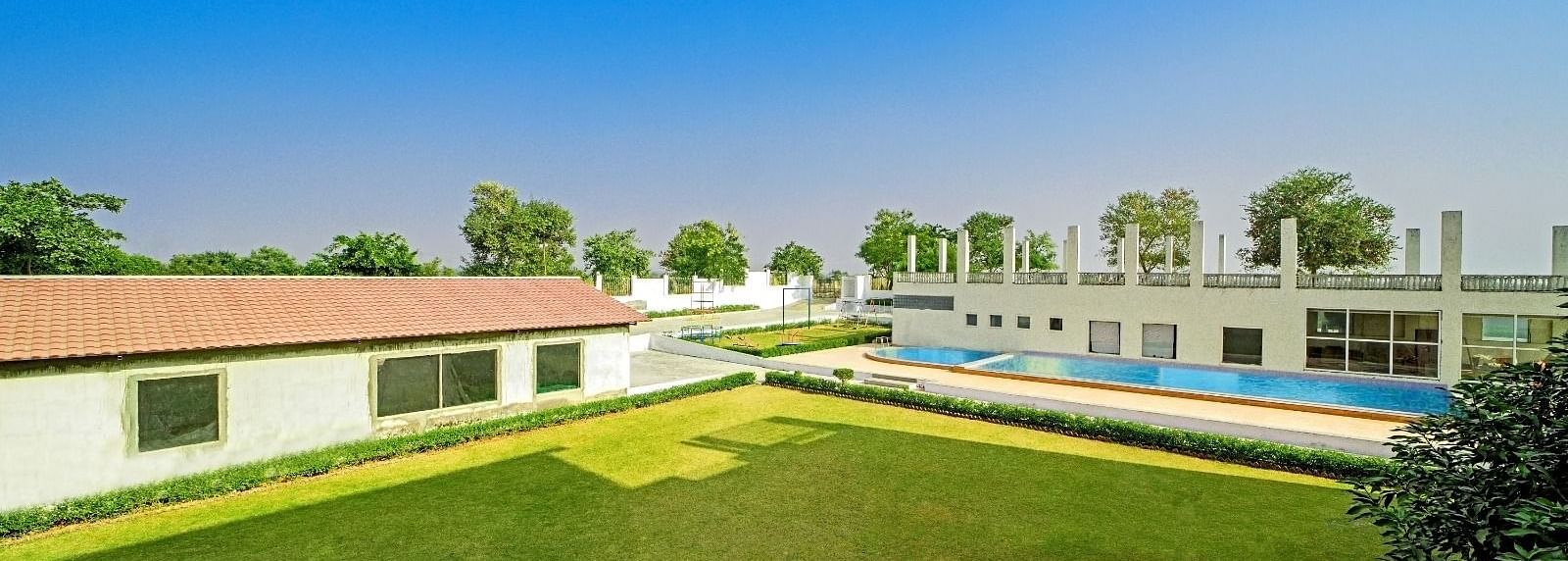 Expansive lawn with a swimming pool and buildings in the background at Grassfield Riveria Resort, Jaipur.