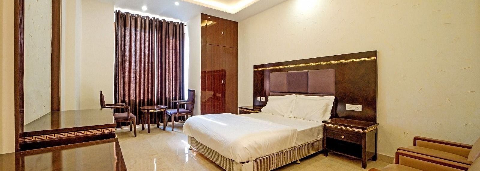 Elegant bedroom at Grassfield Riveria Resort, Jaipur, featuring a large bed, wooden furniture, and warm ambient lighting.