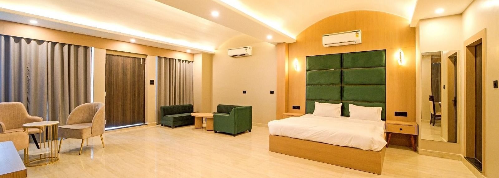 Spacious bedroom at Grassfield Riveria Resort, Jaipur, featuring a large bed, seating area, modern lighting, and floor-to-ceiling curtains.