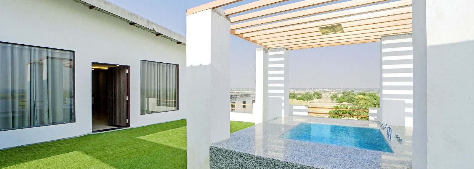 Poolside lounge area at Grassfield Riveria Resort, Jaipur, featuring a shaded seating space and views of the swimming pool.