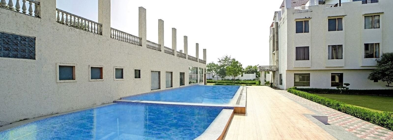 Outdoor swimming pool at Grassfield Riveria Resort, Jaipur, featuring clear water and a wooden deck under bright sunlight.