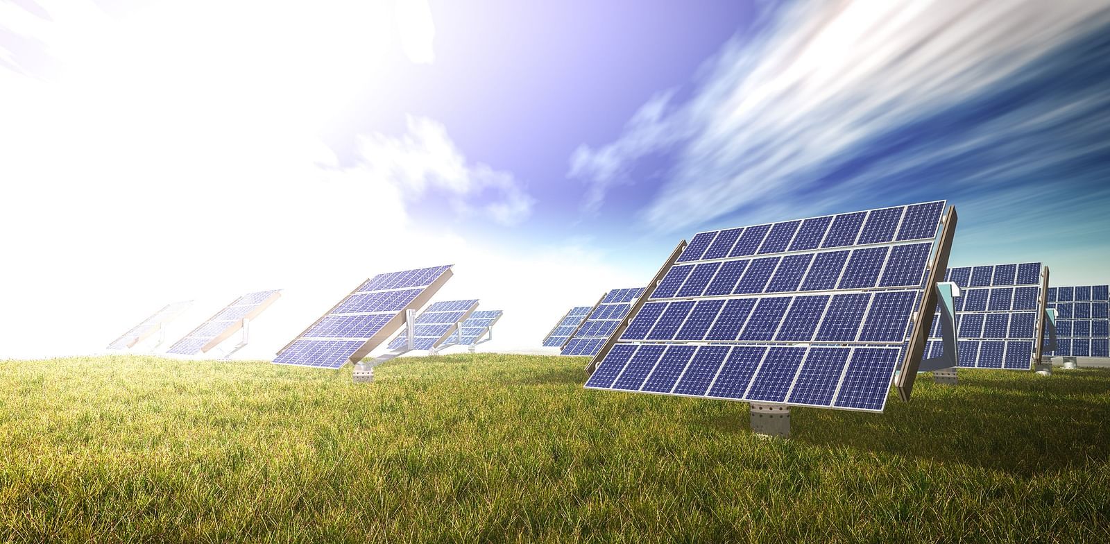 Solar panels in a field under a bright sky with wispy clouds.