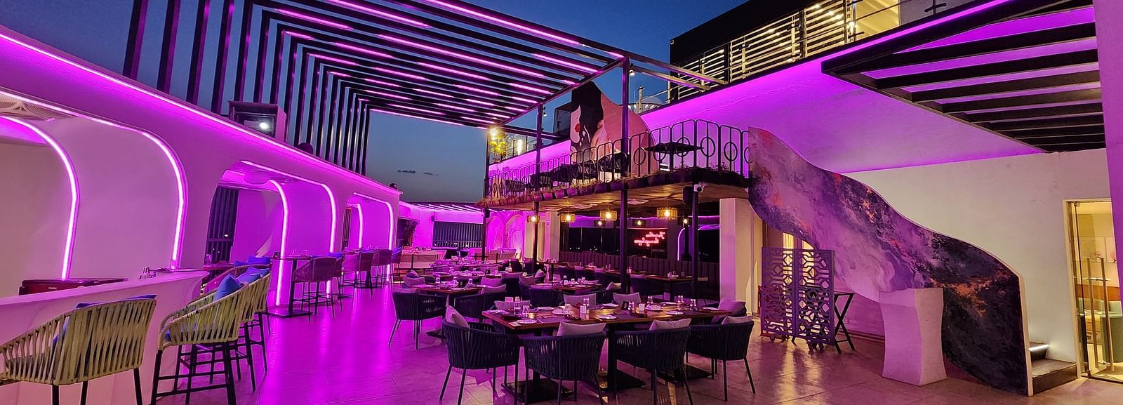 wide angle shot of the rooftop dining area at Lords Inn Rajkot with variously arranged dining area on the floor, a balcony with seating area, and  a dimly lit ambience