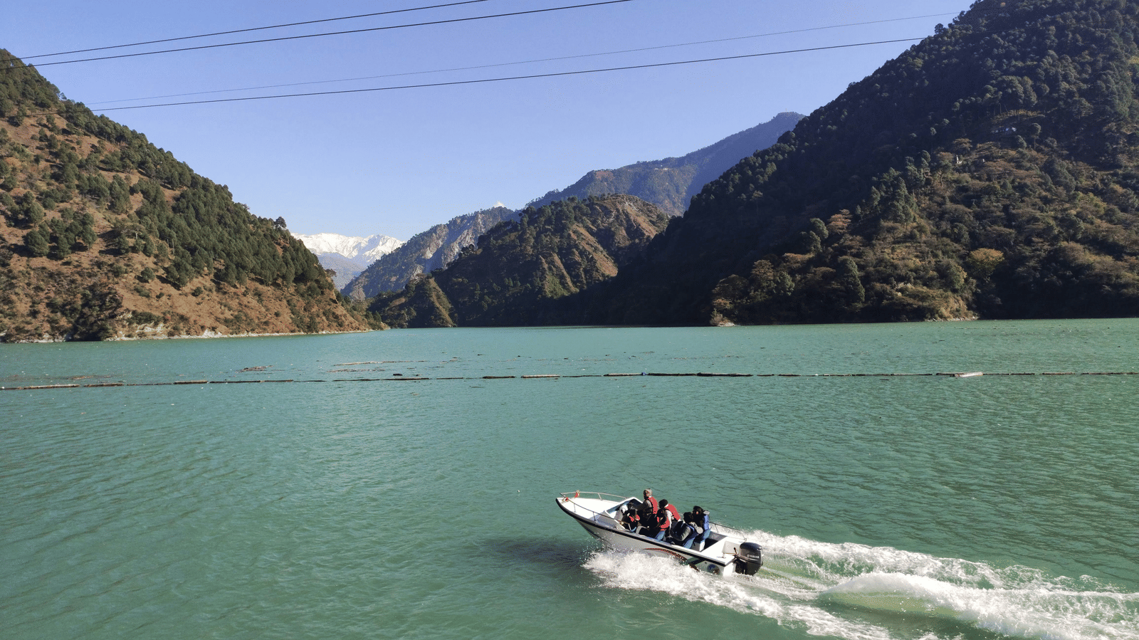 A person riding on a speedboat across a vast lake embraced by towering mountains.