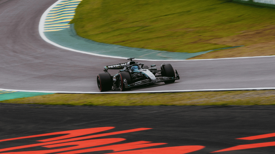 A view of a Mercedes F1 car moving through the turns in the Doha Grand Prix with grass and apex on either side of the road.