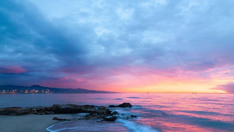 The sky lit up in vibrant colours at the beach, reflecting over the water as the sun sets