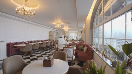 Sun-lit dining area with chandeliers, white tables, and cushioned booths - Mayfair Cafe & Suites, Dalhousie