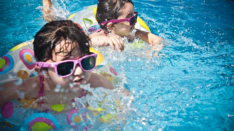 Children are enjoying themselves in the pool, floating on their inflatables and wearing sunglasses, soaking up the fun and sun.