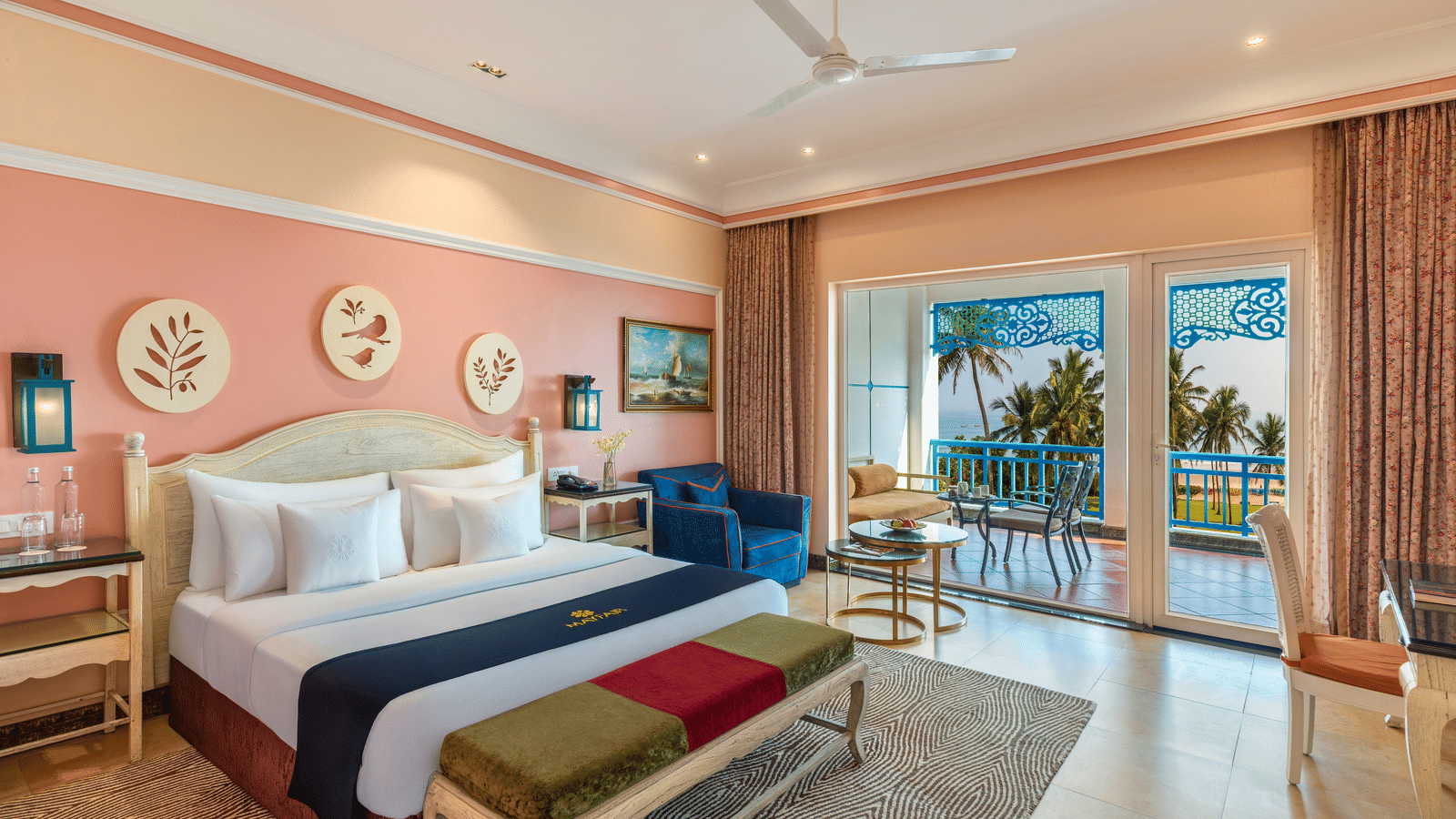 Deluxe room with a king bed, a bench, an armchair and a balcony overlooking the sea and palm trees at MAYFAIR Palm Beach Resort, Gopalpur-on-Sea.