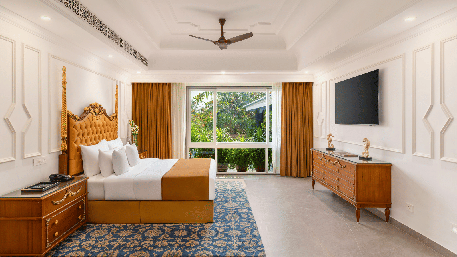 Honeymoon villa with a carved wooden four-poster bed, a dresser, a wall-mounted television and a garden-facing window at MAYFAIR Palm Beach Resort, Gopalpur-on-Sea.