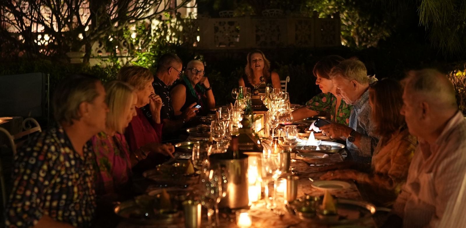 A group of guests enjoy an intimate candlelit dinner outdoors, surrounded by nature at night - Khas Bagh, Jaipur.