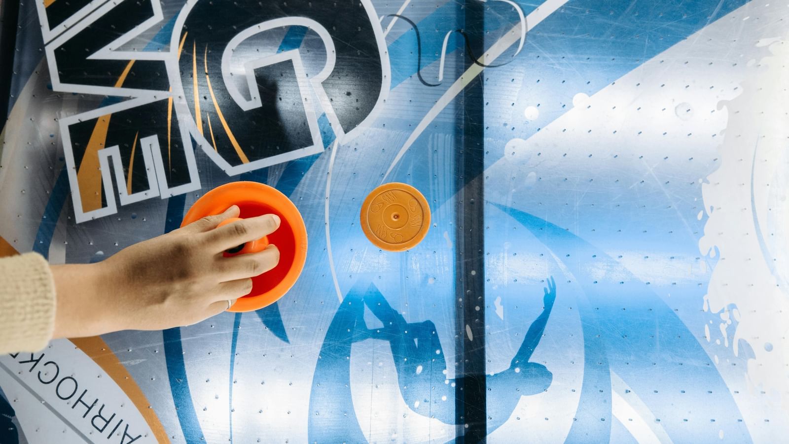 A person moving an air hockey disc on a table