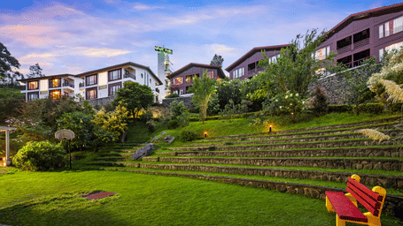 Exterior view of GReaT trails Kodaikanal by GRT Hotels in Kodaikanal at dusk, featuring hillside cottages, landscaped gardens, and illuminated pathways.