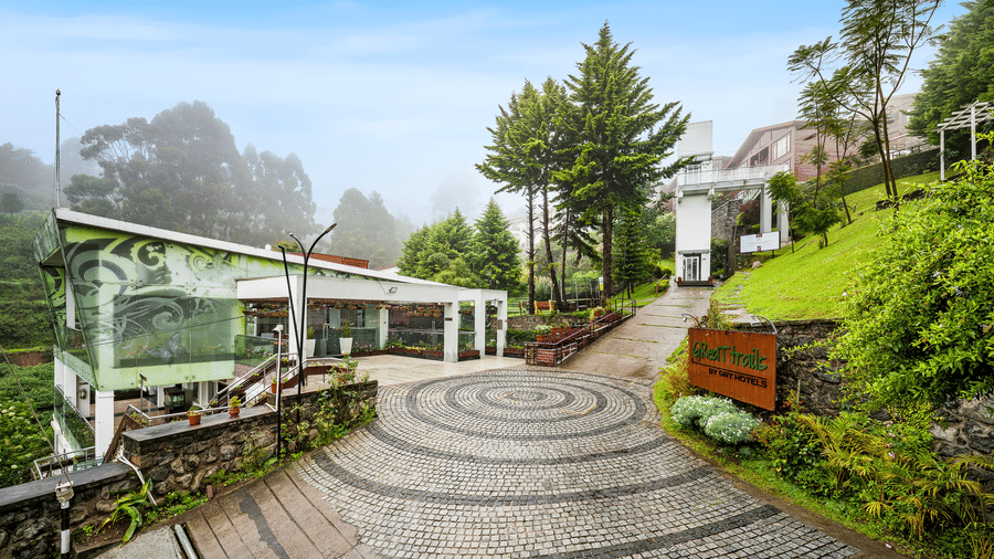 A wide-angle shot of the paved driveway at the entrance of GReaT Trails Kodaikanal By GRT Hotels, surrounded by lush greenery and the trails leading to the best mountain view resort in Kodaikanal, Tamil Nadu.