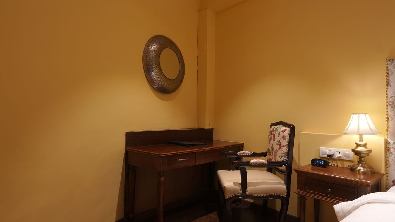 A wooden work desk and a chair with a wall clock and a side table at the Suite Cottage Room at The Garden Ananta Elite Rajkot 7