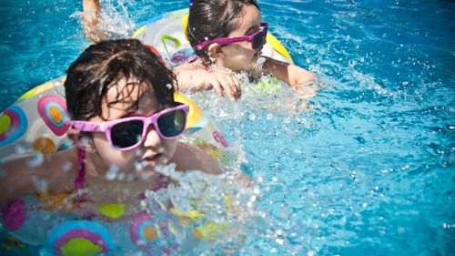 Two children playing in the swimming pool, wearing sunglasses and floaties.