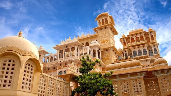 An intricately carved palace with a tree in front of it and blue sky in the background - Chunda Hotels