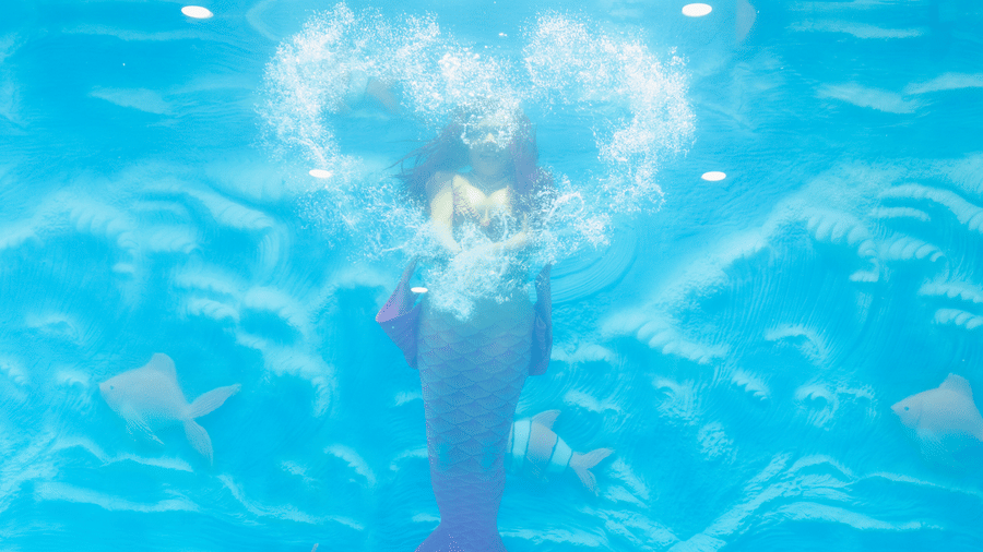 A swimmer moves gracefully underwater in a clear blue pool, surrounded by shimmering bubbles.