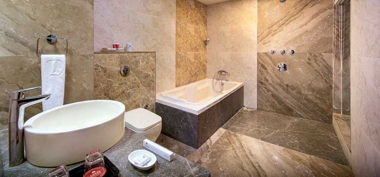A clean and modern hotel bathroom includes a soaking bathtub, a contemporary washbasin, and tiled walls with shower fixtures.