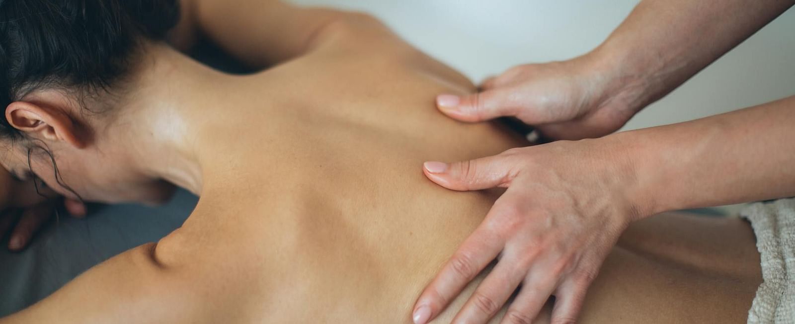A lady laying faced down on a spa table receiving a back massage with oil