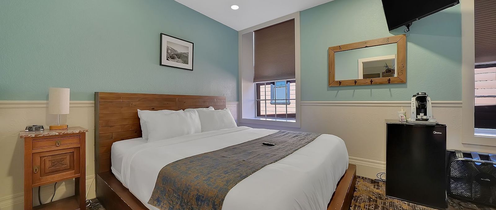 A comfortable room at The Groveland Hotel with sage green walls, wooden bed, blue patterned runner, TV, and convenient coffee station.