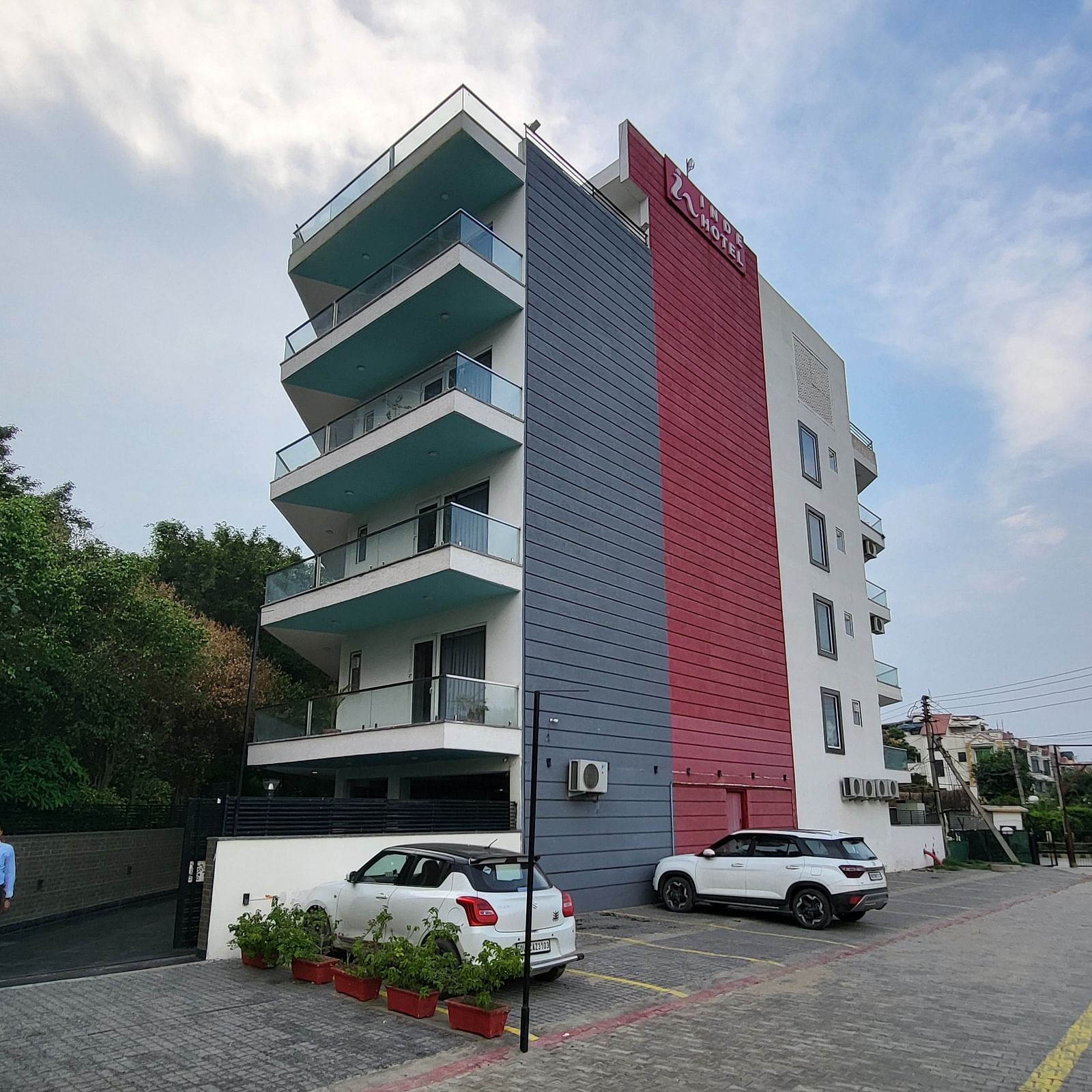 A facade of Inde Hotel Golf Course Extension featuring multiple storeys and balconies on each floor, and cars parked on the lawn