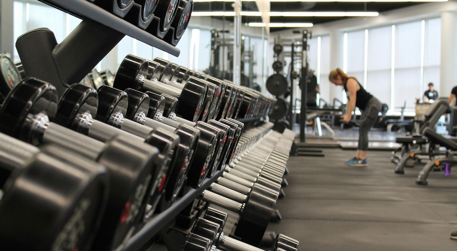 A close up shot of dumbbells in a rack with a person in the background working out