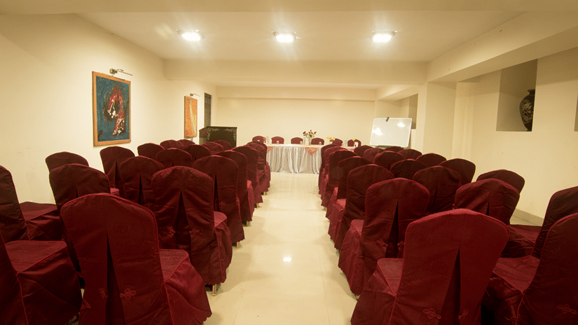 Conference hall with rows of red chairs facing the stage with a panel at Central Hill Resort, one of the best hotel near MG Marg.