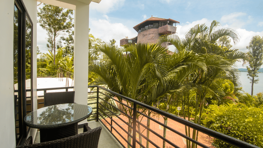 Image of a balcony with two chairs and a table with a view of the nature surrounding it at Coorg Jungle Camp Backwater Resort, Kushalnagar.