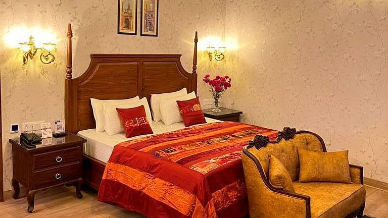 Elegant bedroom at Hotel Mount View featuring a wooden four-poster bed with vibrant red linens, ornate chandelier, floral wallpaper, side tables, cosy upholstered seating.