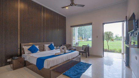 Full view of the Deluxe Room with ample of natural light coming from the outside featuring a double bed, overlooking the lush green lawn from the window and the entrance.