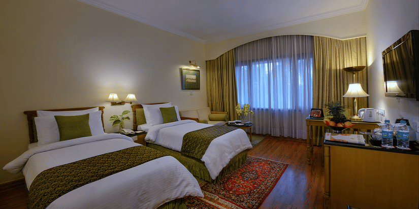 A Standard Room at The Clarks Varanasi featuring twin beds with matching rugs, full-length curtains and a flat-screen television.