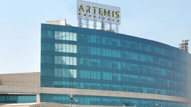 Multiple storey Artemis Hospital building exterior featuring a parking area and landscaped greenery.