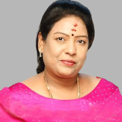 A woman in a bright pink outfit with a bindi, smiling against a grey background - Kaldhan Samudhra Palace