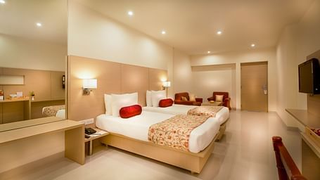 An image of a king size bed with a work desk and TV of a Suite at Regency Tiruttani by GRT Hotels.