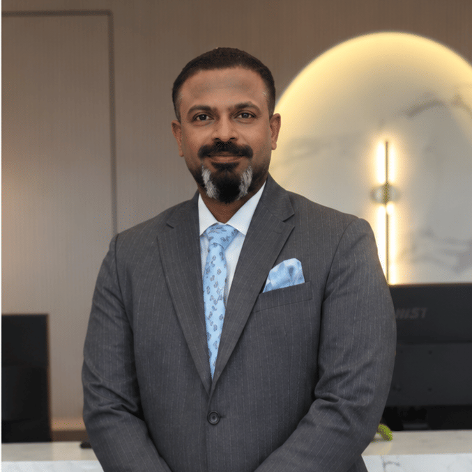Portrait of Shibu Jacob, Corporate Head of Food and Beverage at Pride Hotel Group, in a grey suit at a hotel interior setting.